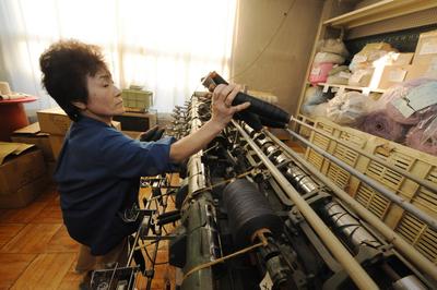 An elderly Japanese worker creates fine yarn on an old yarn machine at the Sato Seni Co. Ltd. factory, a knitware wholesale manufacturing company located in Sagae city, Yamagata province in northern Japan, 22 October 2009. (Photo: AAP)
