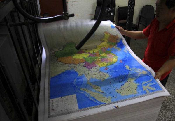 A printing worker holds a new officially approved map of China that includes the islands and maritime area that Beijing claims in the South China Sea, at a factory in south China's Hunan province on 27 June 2014. (Photo: AAP).