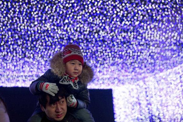 A man carries a child on his shoulders as they visit an annual lights festival held at a shopping mall in Beijing, 27 December 2014. The month long festival spans Christmas and New Year, giving retailers a chance to boost sales as they ring in the New Year. (Photo: AAP).