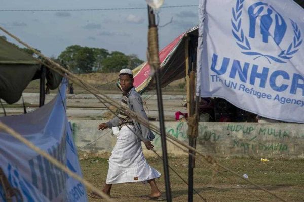 A Rohingya migrant walks past the UNHCR flag at a confinement area in Kuala Cangkoi in Aceh. More than 3,500 migrants including Bangladeshi and Rohingya from Myanmar have swum to shore or been rescued off the coasts of Malaysia, Indonesia, Thailand and Bangladesh since the migrant crisis erupted early May 2015. (Photo: AAP)