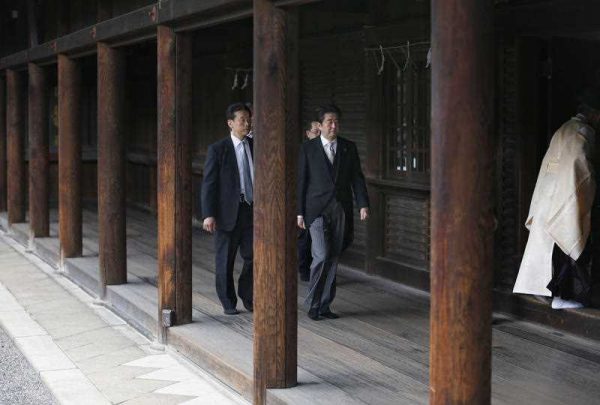 Japanese Prime Minister Shinzo Abe, second from left, is led by a Shinto priest, right, after paying respect for the war dead at Yasukuni Shrine in Tokyo (Photo: AAP)