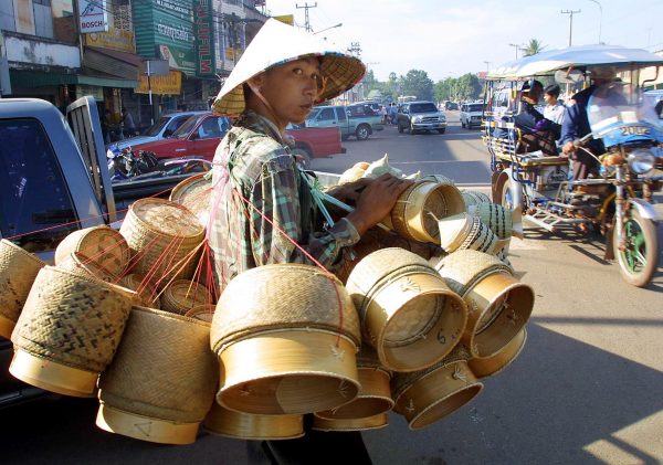 A bamboo basket vendor walks across a busy street in Vientiane, Laos. The poverty in the countryside area has forced many people to come seeking jobs with better income in the capital where many of them work as street vendors (Photo: AAP).