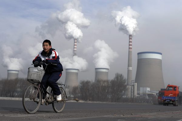 A Chinese boy cycles past a cooling towers of a coal-fired power plant in Dadong, Shanxi province, China. (Photo: AAP)