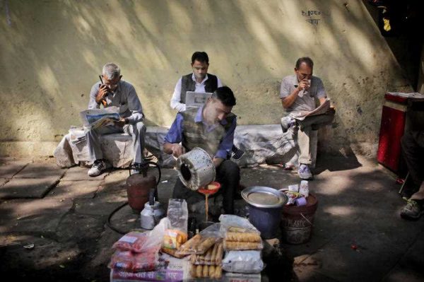An Indian roadside tea vendor prepares tea for people reading newspapers in New Delhi, India, Tuesday, 1 March 2016. (Photo: AAP).