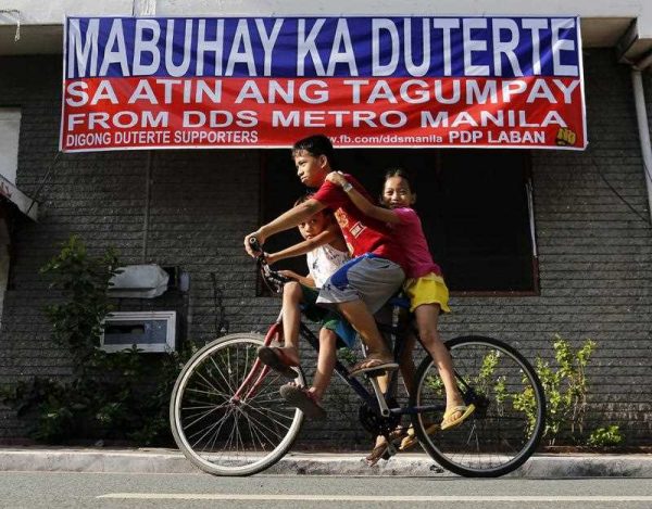 Filipino children riding on a bicycle pedal past a banner, reading 'Long Live Duterte! We are the winners!’ in Manila, 29 June 2016. (Photo: AAP)