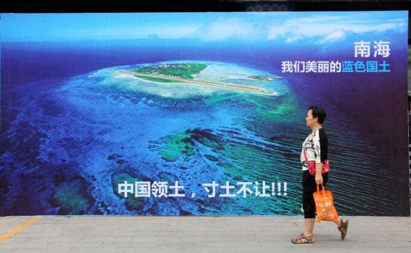 A pedestrian walks past a photo showing Yongxing Island in the South China Sea on a street in Weifang city, Shandong province, China, 14 July 2016. (Photo: AAP).