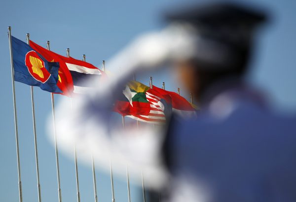 A police officer stands near national flags of ASEAN counties during the 25th ASEAN Summit in Myanmar. (Photo: Reuters).