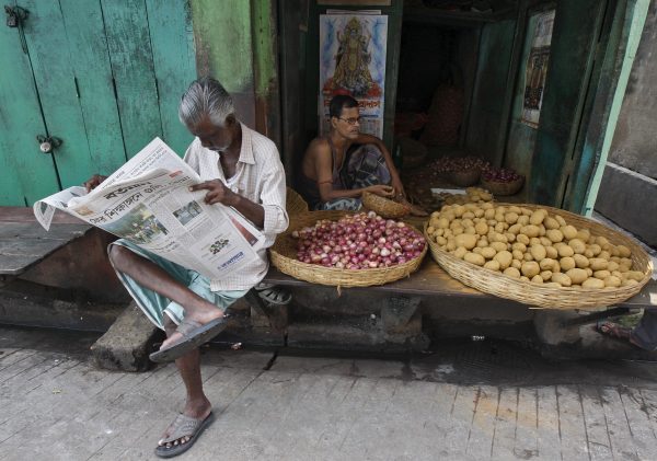 A local resident reads a newspaper next to a vendor selling potatoes and onions at a slum area in Kolkata, India. (Photo: Reuters).