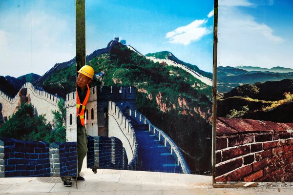 A worker looks through the fence of a construction site that is decorated with pictures of the Great Wall at Badaling, north of Beijing, China, 1 September 2016. (Photo: Reuters/Thomas Peter).