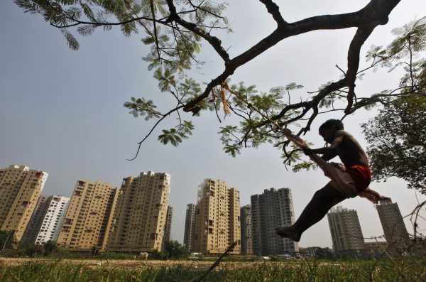 A boy plays on a swing suspended from a tree in front of a residential estate under construction in Kolkata, India, 31 October 2011. (Photo: Reuters/Rupak De Chowdhuri).