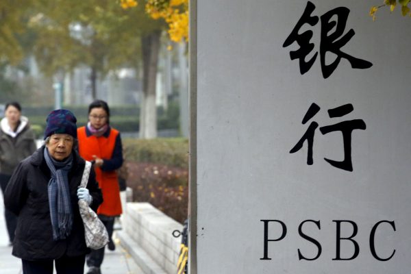 People walk past a sign outside a branch of Postal Savings Bank of China (PSBC) in downtown Beijing, China, 12 November 2015. (Photo: Reuters/Kim Kyung-Hoon).