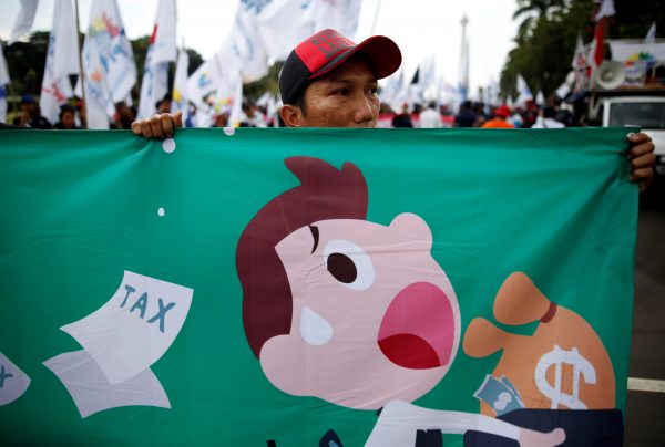 A protester holds a banner at the start of an Indonesian union workers' protest against a government tax amnesty near the presidential palace in Jakarta, Indonesia (Photo: Reuters/Darren Whiteside).