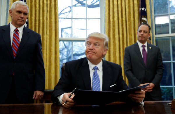 US President Donald Trump, flanked by Vice President Mike Pence and White House Chief of Staff Reince Priebus, looks up while signing an executive order in the Oval Office of the White House in Washington, 23 January 2017. (Photo: Reuters/Kevin Lamarque).