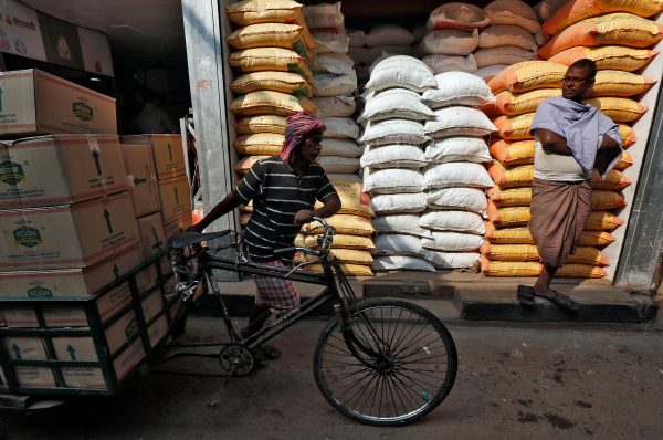 A labourer carries vegetable oil packets on a tricycle as a man stands in front of his shop selling food grains, at a wholesale market in Kolkata, India, 4 January, 2017. (Photo: Reuters/Rupak De Chowdhuri).
