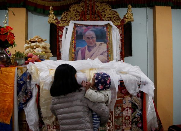 A Tibetan woman carrying a child offers prayer on the portrait of exiled Tibetan spiritual leader, the Dalai Lama, during a function to mark the Tibetan Uprising Day at the Tibetan Refugee camp in Lalitpur, Nepal 10 March 2017 (Photo: Reuters/Navesh Chitrakar).