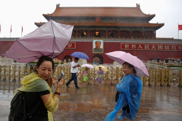 Tourists hold umbrellas as they stand in front of the Tiananmen Gate and a giant portrait of Chinese late Chairman Mao Zedong on a day of heavy rain in Beijing, China, 20 July 2016 (Photo: Reuters/Thomas Peter).