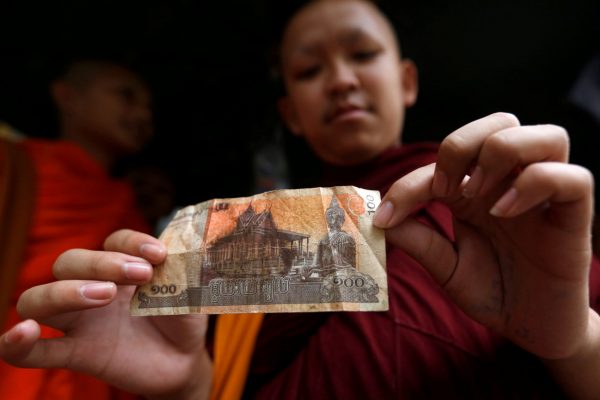 A Buddhist monk holds a riel banknote with the image of Buddha at a store in Phnom Penh, Cambodia, 22 August, 2017 (Photo: Reuters/Samrang Pring).