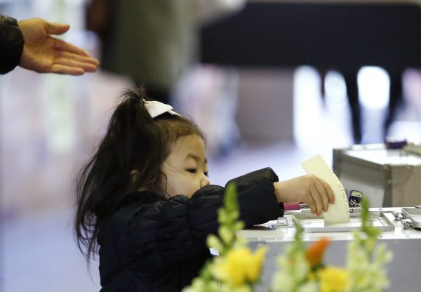 A child casts an adult's ballot paper at a polling station as part of Japan's general election in Tokyo, 14 December 2014 (Photo: Reuters/Thomas Peter).