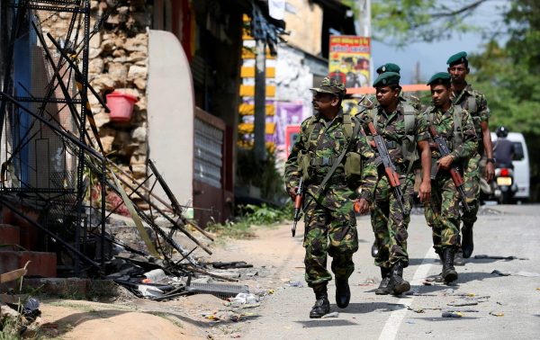 Sri Lanka's Special Task Force soldiers walk past a damaged houses after a clash between two communities in Digana central district of Kandy, Sri Lanka, 8 March 2018 (Photo: Reuters/Dinuka Liyanawatte).