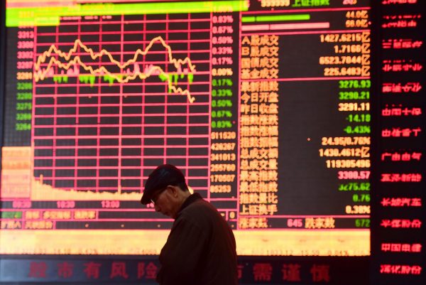 A man is seen against an electronic board showing stock information at a brokerage house in Fuyang, Anhui province, China, 16 March 2018 (Photo: Reuters/Stringer).