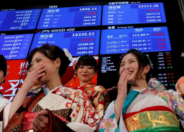 Women, dressed in ceremonial kimonos, smile in front of an electronic board displaying the Nikkei average as they pose after the ceremony that kicks off the first day of trading in 2018 at the Tokyo Stock Exchange in Tokyo, Japan, 4 January 2018 (Photo: Reuters/Kim Kyung-Hoon).