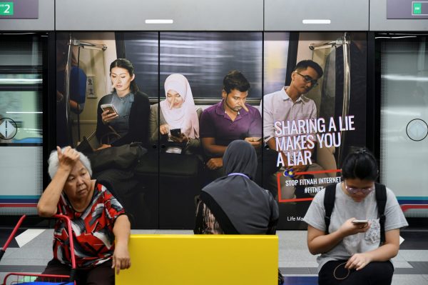 Commuters sit in front of an advertisement discouraging the dissemination of fake news at a train station in Kuala Lumpur, Malaysia on 28 March 2018. (Photo: Reuters/Stringer).