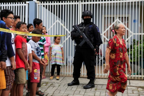 An anti-terror policeman stands guard during a raid of a house of a suspected terrorist as people watch at Medokan Ayu area in Surabaya, Indonesia, 15 May 2018 (Photo: Reuters/Beawiharta).