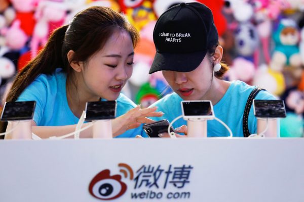 Members of staff use a smartphone at Sina Weibo's booth during Global Mobile Internet Conference at the National Convention in Beijing, China, 27 April 2018 (Photo: Reuters/Damir Sagolj).