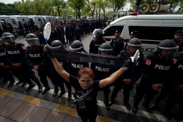 An anti-government protester stands in front of riot police officers during a protest to demand that the military government hold a general election by November, in Bangkok, Thailand, 22 May 2018 (Photo: Reuters/Athit Perawongmetha).
