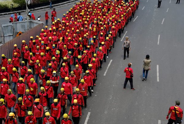 A police officer walks beside a group of Indonesian workers marching to mark May Day in Jakarta, Indonesia, 1 May 2017 (Photo: Reuters/Beawiharta).