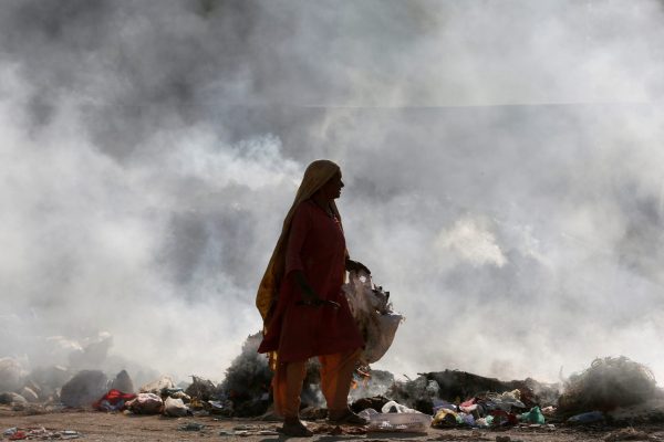 An elderly woman walks as she searches for recyclables from the smouldering dump along a road in Karachi, Pakistan, 8 December 2017 (Photo: Reuters/Akhtar Soomro).