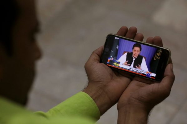 A journalist poses with a cell phone displaying Pakistan’s Prime Minister Imran Khan speaking to the nation in his first televised address, Karachi, Pakistan 19 August 2018 (Photo: Reuters/Akhtar Soomro).