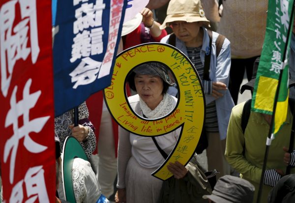 A protester holding a placard featuring Japan's war-renouncing Article 9 marches during an annual May Day march organized by the Group of the National Confederation of Trade Unions, commonly known in Japanese as Zenroren, in Tokyo, 1 May 2015. Thousands of union workers and activists gathered and marched central Tokyo on International Workers' Day, also known as Labour Day or May Day, to demand higher pay and better working conditions, a halt to nuclear power plants, and protested against war and Japan's Prime Minister Shinzo Abe's administration (Photo: Reuters/Issei Kato).