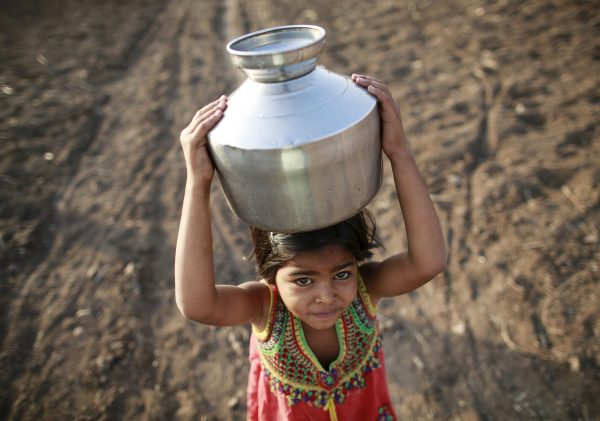 A girl carries a metal pitcher filled with water through a field in Latur, India, 17 April 2016, (Photo: Reuters/Danish Siddiqui).