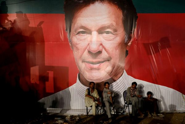 Labourers, who set up the venue, sit under a wall with a billboard displaying a photo of Imran Khan, chairman of the Pakistan Tehreek-e-Insaf political party, as they listen to him during a campaign rally ahead of general elections in Karachi, Pakistan, 22 July 2018 (Photo: Reuters/Akhtar Soomro).