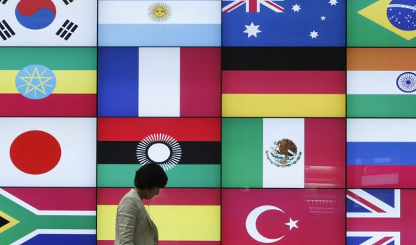 A woman walks by a signboard showing flags of the participating countries for the then-upcoming G20 Seoul summit at the venue of the summit in Seoul, South Korea, 4 November 2010 (Photo: Reuters/Truth Leem).