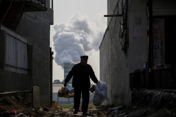 A man collects recyclables from an alley as smoke billows from the chimney of a factory in rural Gaoyi county, known for its ceramics production, near Shijiazhuang, Hebei province, China, 7 December 2017 (Photo Reuters/Thomas Peter).