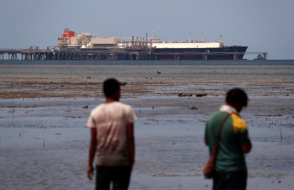 Locals walk along a small beach where a Liquefied Natural Gas carrier called Kumul is docked at the marine facility of the ExxonMobil PNG Limited operated LNG plant at Caution Bay, located on the outskirts of Port Moresby in Papua New Guinea, 19 November 2018 (Photo: Reuters/David Gray).