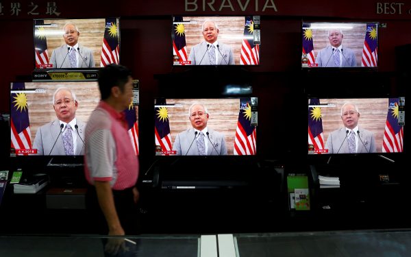 A man passes a live telecast of Malaysia's Prime Minister Najib Razak addressing the nation on the dissolution of Parliament at an electronics shop in Port Klang, Malaysia, 6 April 2018 (Photo: Reuters/Lai Seng Sin).