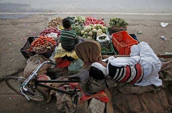 A vendor sleeps as his son waits for customers at their roadside vegetable shop in New Delhi, India, 12 February 2019 (Photo: Reuters/Adnan Abidi).