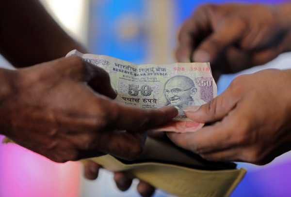 A customer hands a 50-Indian rupee note to an attendant at a fuel station in Ahmedabad, India, 5 October 2018, (Photo: Reuters/Amit Dave).