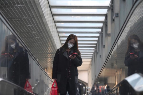 A woman wearing a face mask looks at her phone while riding an escalator, following an outbreak of the novel coronavirus in the country, in Beijing, China 23 February, 2020 (Reuters/Stringer).