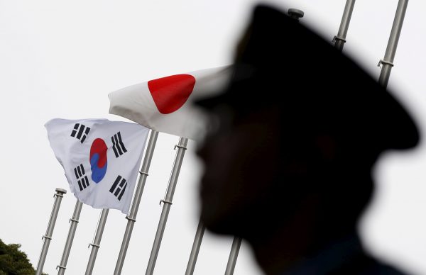 A police officer stands guard near Japanese and South Korean national flags during a reception to mark the 50th anniversary of normalisation of ties between the two countries, Tokyo, Japan, 22 June 2015 (Photo: Reuters/Toru Hanai).