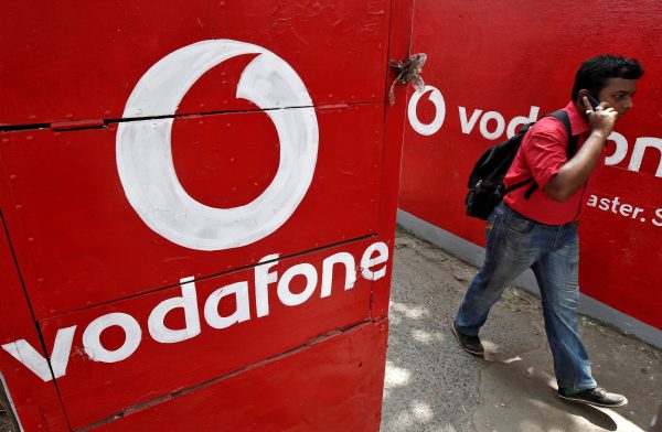 A man and two passengers ride on a scooter past a shop displaying the Vodafone logo on its shutter in Jammu (Photo: Reuters/Mukesh Gupta).