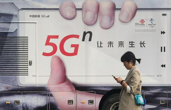 A woman using her mobile phone walks past a vehicle covered in a China Unicom 5G advertisement in Beijing, China 17 September, 2019 (Photo: Reuters/Stringer).