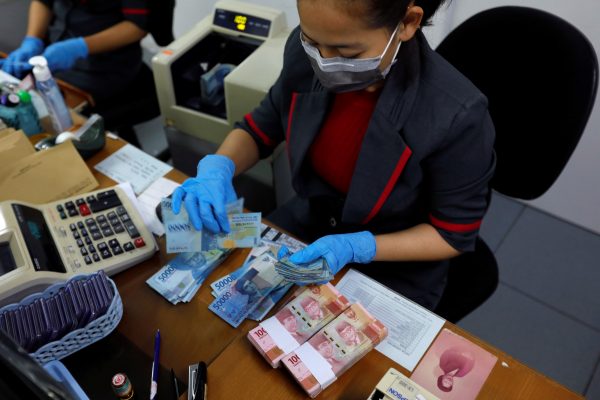 An employee wearing a face mask and synthetic gloves counts Indonesia's rupiah banknotes at a currency exchange office amid the spread of coronavirus disease (COVID-19) in Jakarta, Indonesia, 19 March 2020 (Photo: REUTERS/Willy Kurniawan).