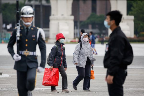 Tourists wear protective face masks to protect themselves from COVID-19 while passing by a flag rising ceremony at Chiang Kai Shek Memorial Hall in Taipei, Taiwan, 11 March 2020 (Photo: Reuters/Ann Wang).