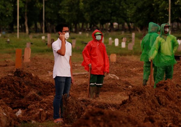 Firos Justin Sumantri, son of Ratih Purwarini, a doctor who passed away due to the coronavirus disease (COVID-19), prays as municipality workers wait, next to his mother's grave during the funeral in Jakarta, Indonesia, 31 March 2020 (Photo: Reuters/Willy Kurniawan).