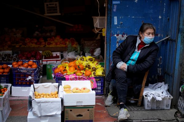 A woman wearing a face mask sits next to a fruit stall at a residential area after the lockdown was lifted in Wuhan, Hubei, 11 April 2020 (Photo: Reuters/Aly Song).