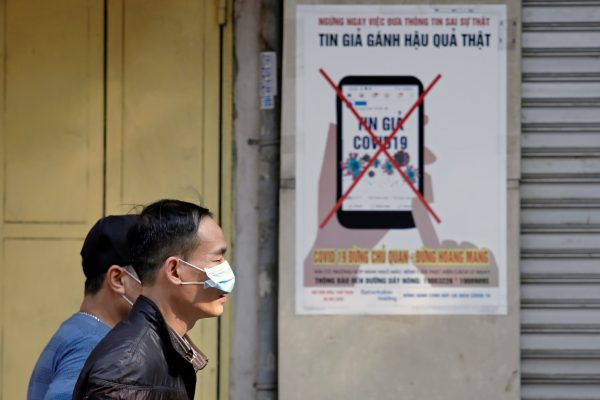 Men wear protective masks as they walk past a poster warning against the spread of ‘fake news’ online on the new coronavirus in Hanoi, Vietnam, 14 April 2020 (Photo: Reuters/Kham).